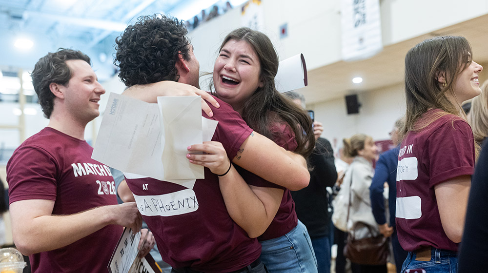 Students wearing maroon t-shirts hugs while one cries tears of joy